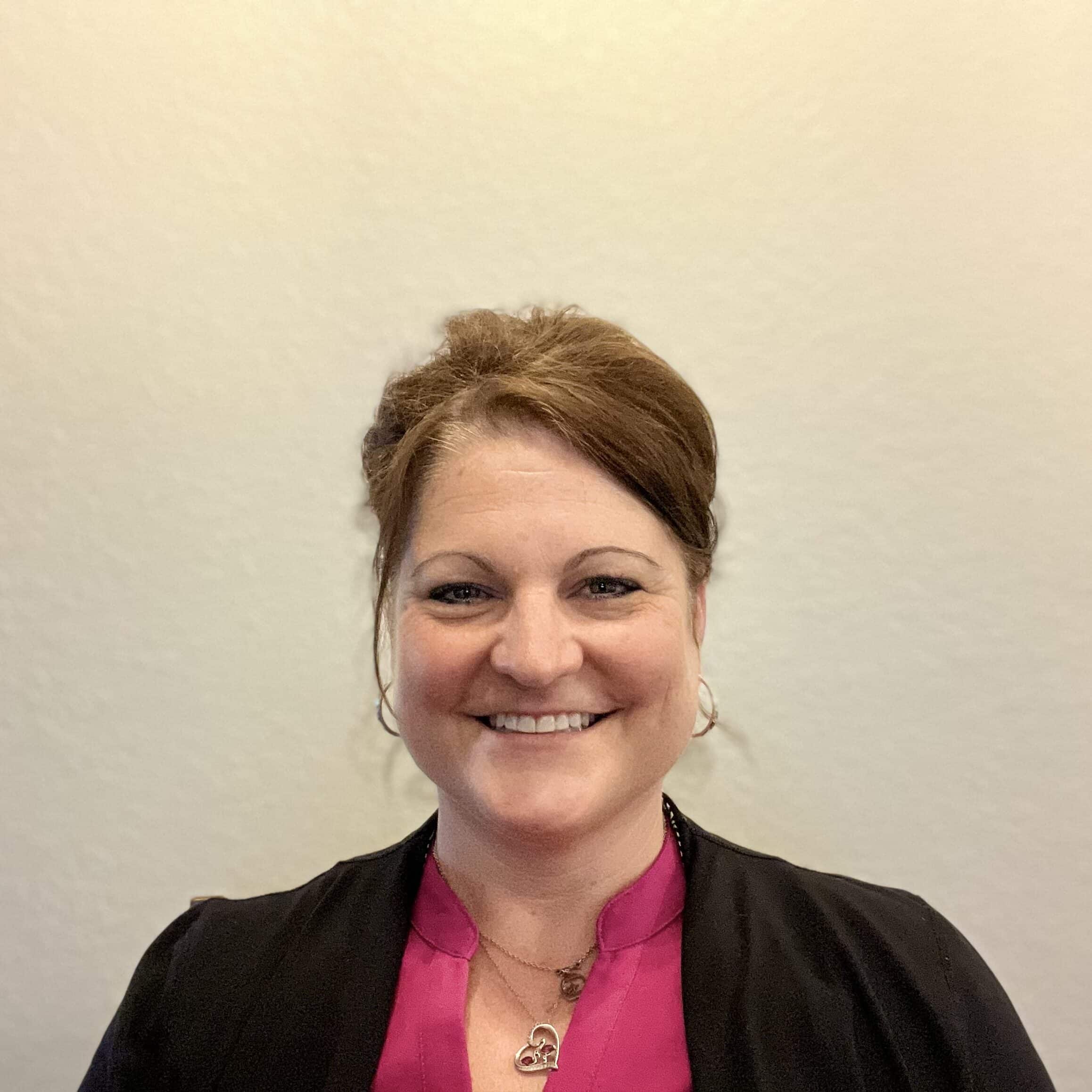 A woman wearing pink and black smiles at the camera against a white background.