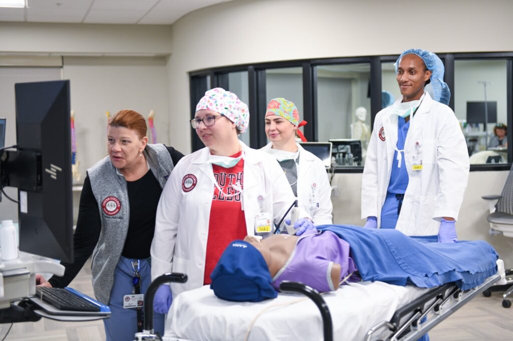 Three Nurse Anesthesia Students with Instructor and Simulated Patient looking at vitas screen